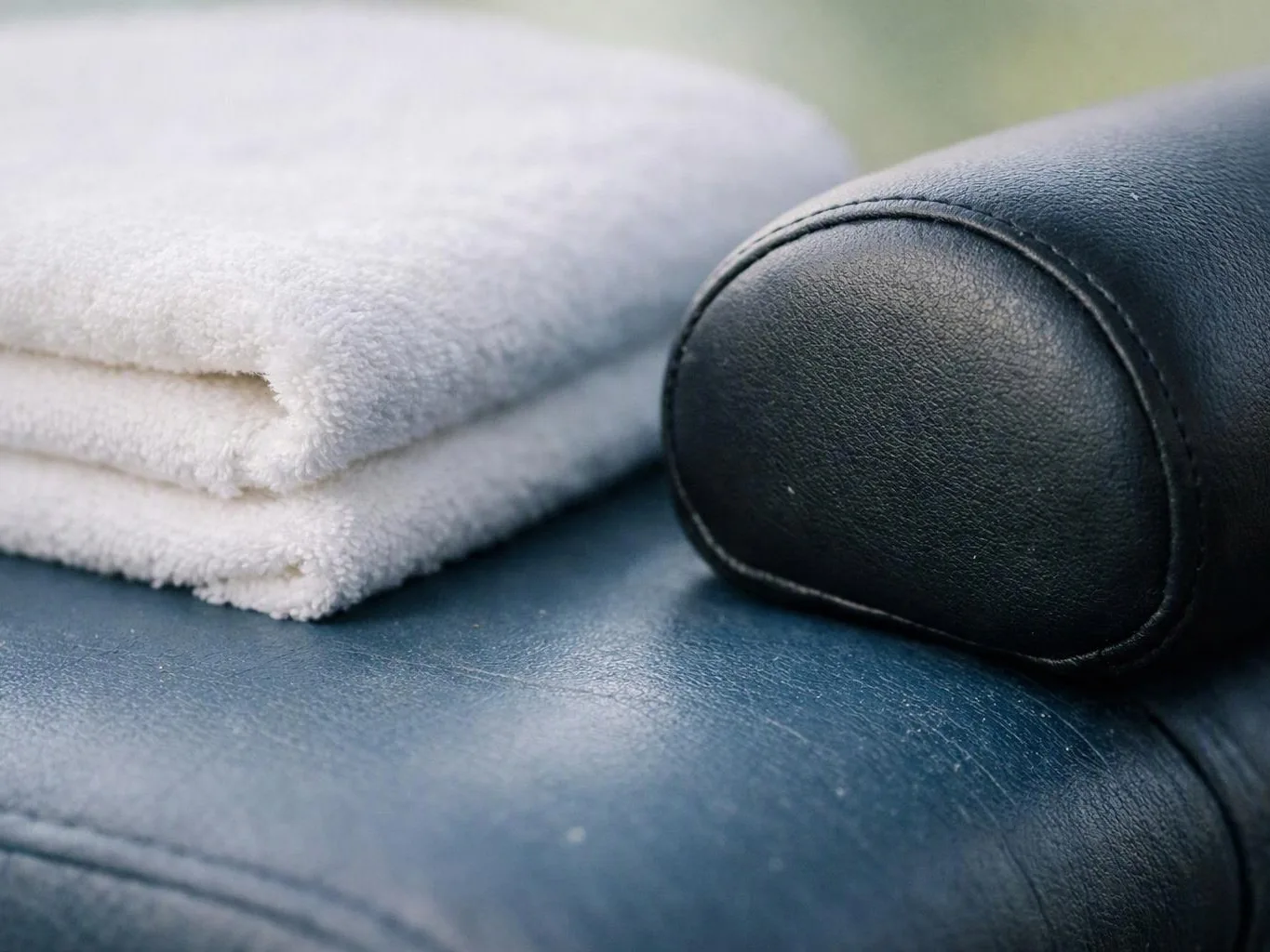 A folded white towel rests beside a black leather armrest on a blue cushioned surface