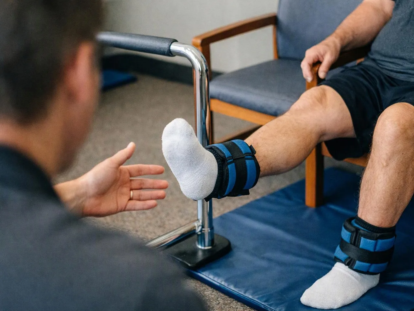 A therapist reaches toward a seated man’s raised leg during a physical therapy exercise in a clinic room