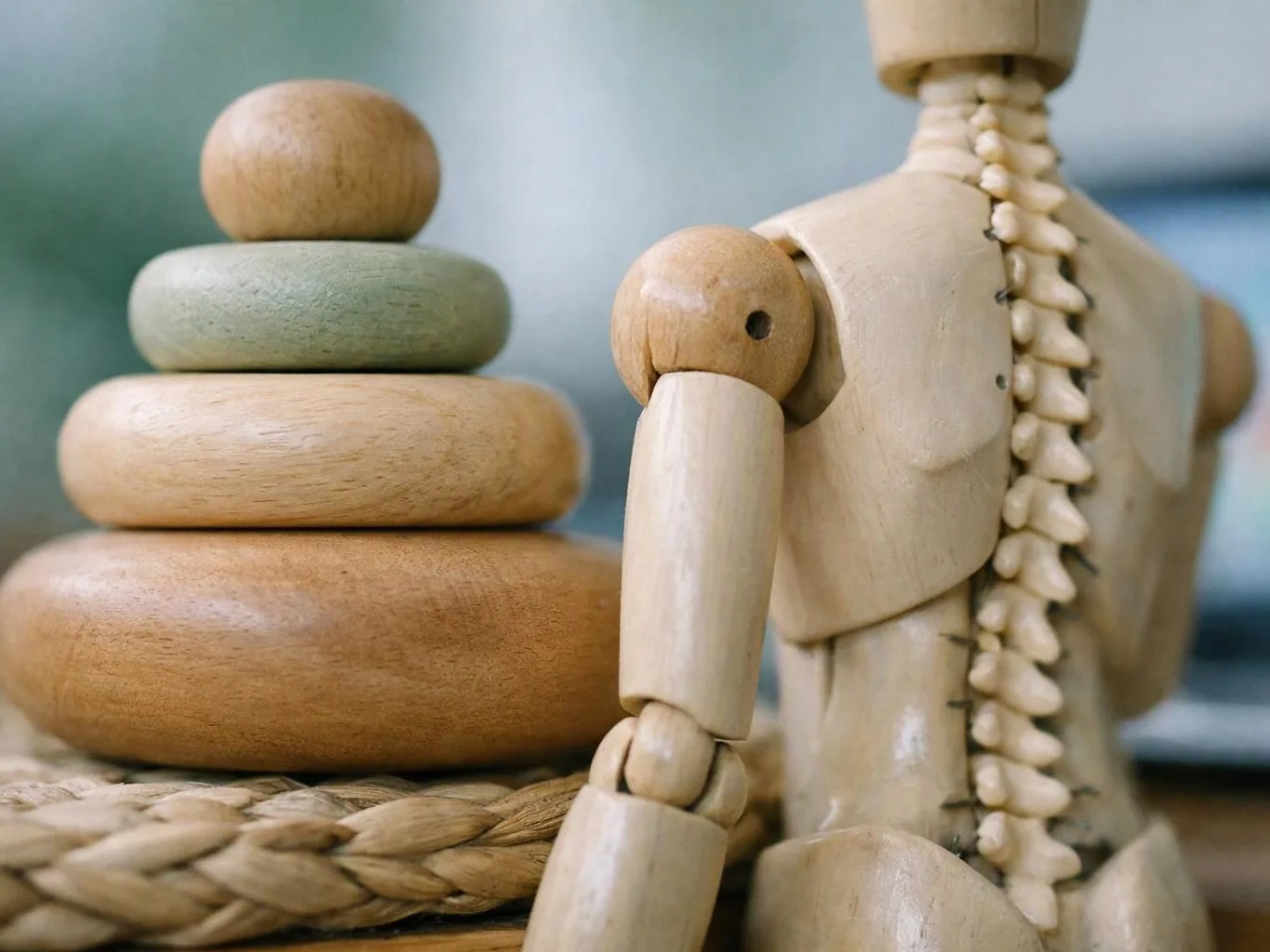 A wooden mannequin stands beside stacked smooth stones on a woven mat
